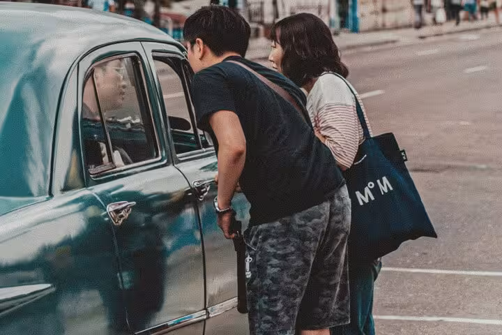Tourists talking with local driver beside vintage cab, starting a classic Muscat private 4 hour sightseeing tour by car