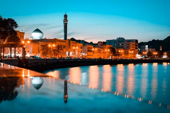 Twilight waterfront skyline of Muscat with illuminated mosque and Corniche, featured stop on private evening city tours