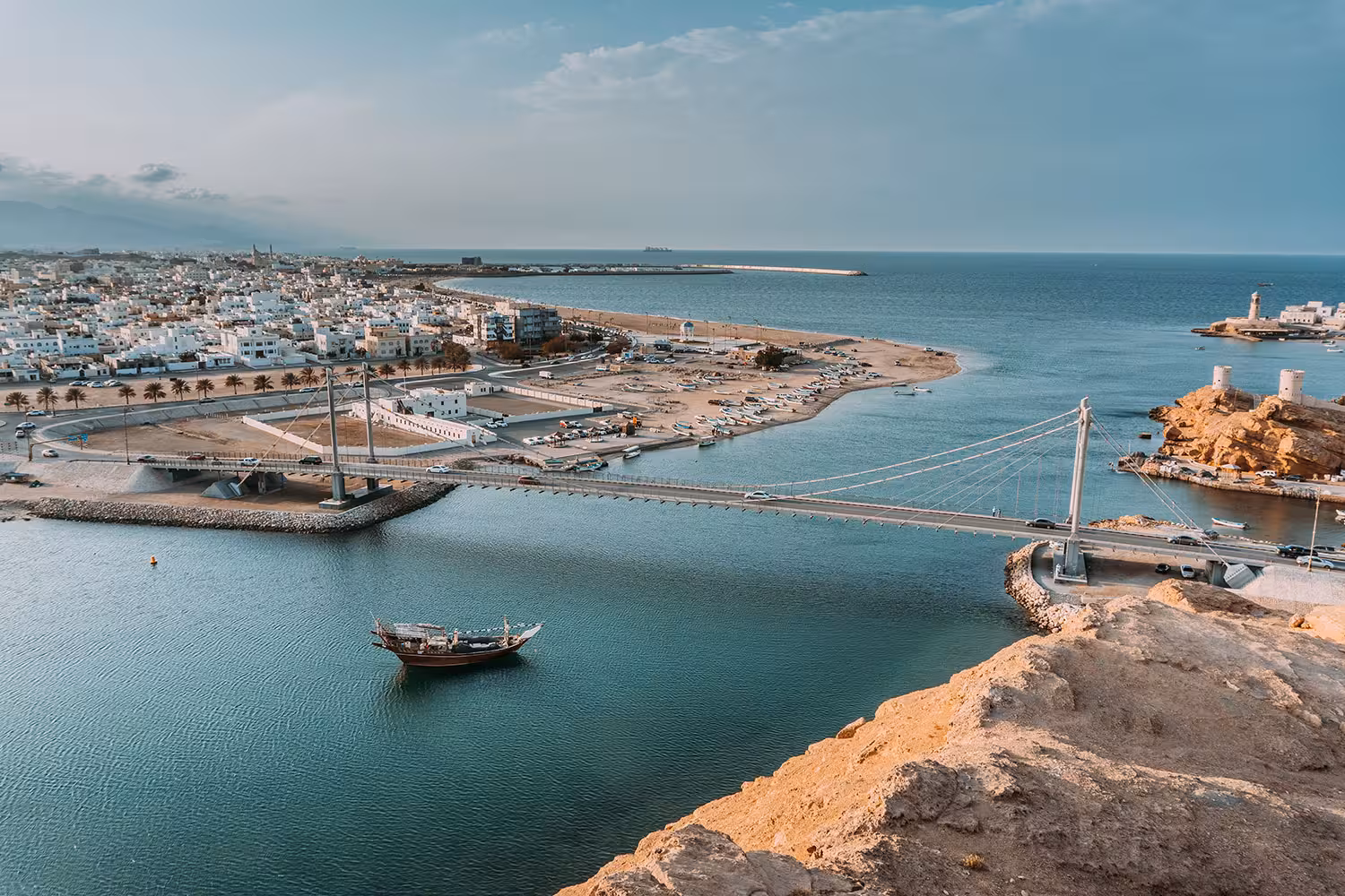 Panoramic view of Sur coastal town, suspension bridge and traditional dhow boat on Muscat to Wadi Shab and turtle tour