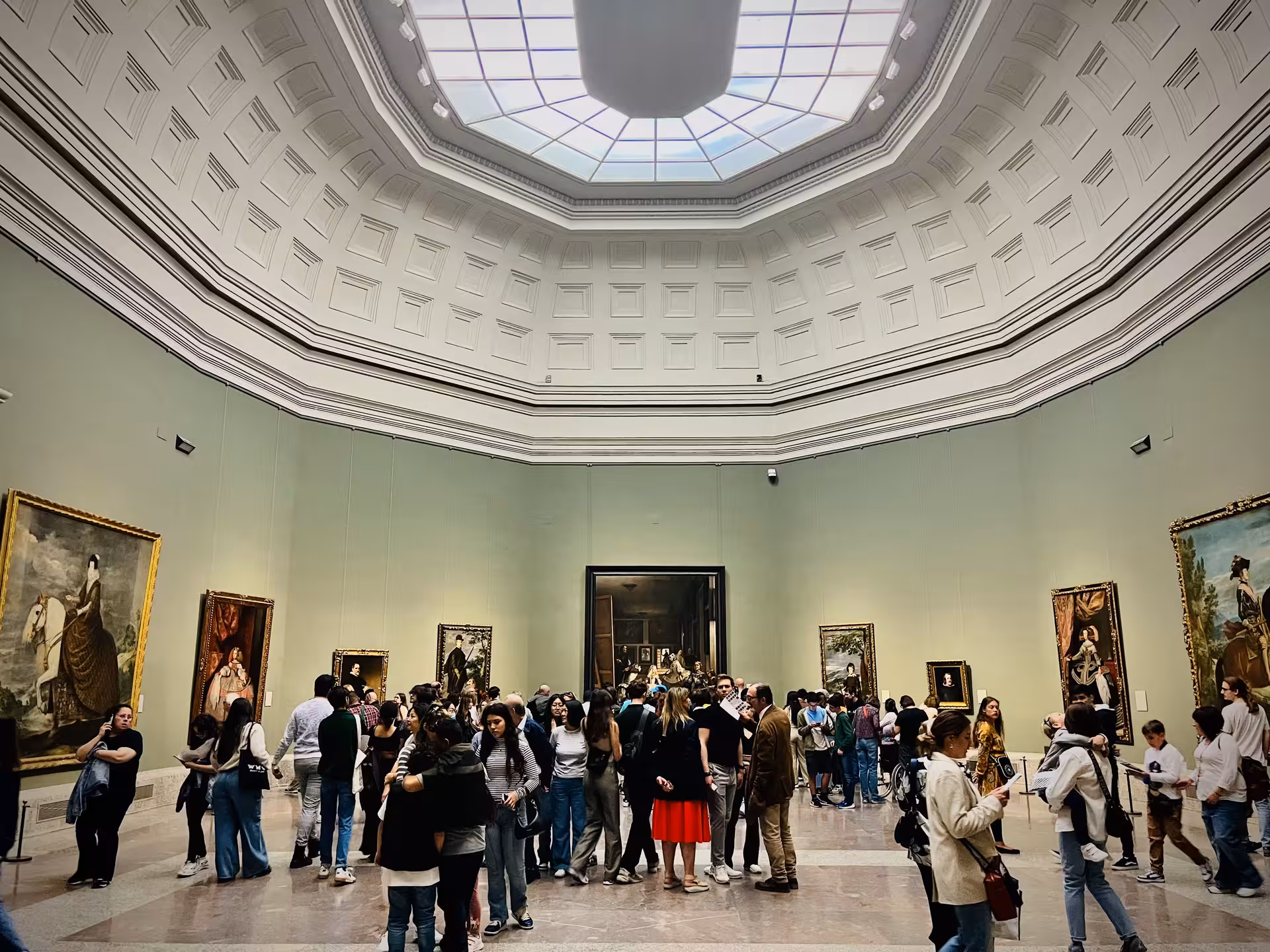 Crowded central hall under skylight at Madrid’s Museo del Prado, visitors viewing iconic paintings on a guided tour