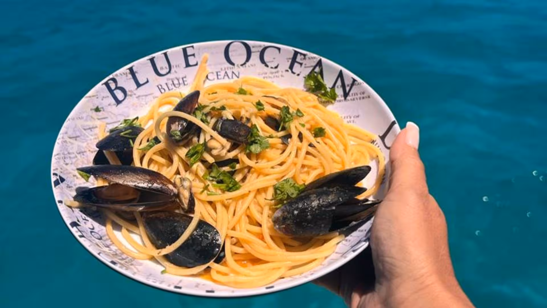 Plate of mussel spaghetti garnished with parsley against the vibrant blue sea in La Maddalena Archipelago tour.