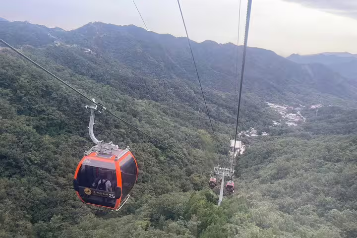 Panoramic vista of cable cars traversing over expansive green landscape on Mutianyu Great Wall private tour by English guide.