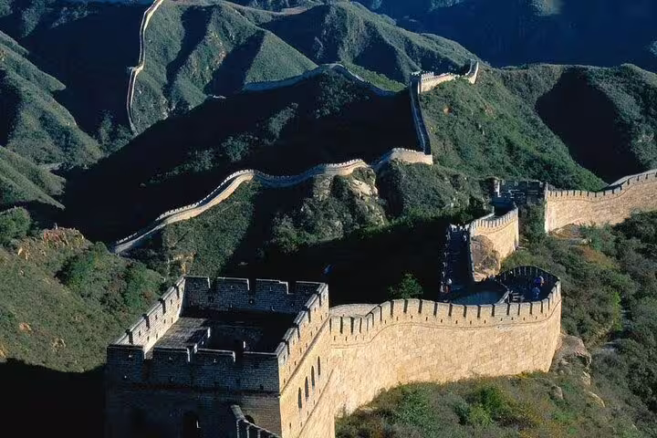 Panoramic view of the Mutianyu Great Wall snaking over lush green hills under a clear blue sky.