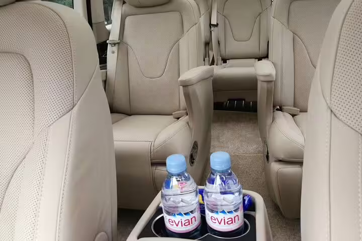 Spacious and comfortable beige interior of a tour van with bottled water, ensuring a relaxing journey to Mutianyu Great Wall.
