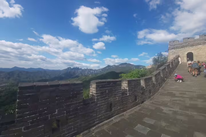 Visitors walking along the Mutianyu Great Wall with scenic mountain views under a bright blue sky.