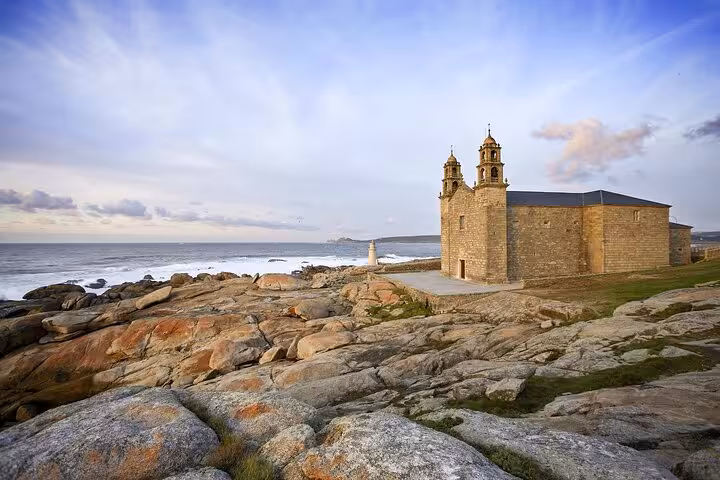 Scenic view of Muxia's coastal church against a rocky shoreline, featured in the Finisterre, Muxia, and Cabo Vilan excursion.