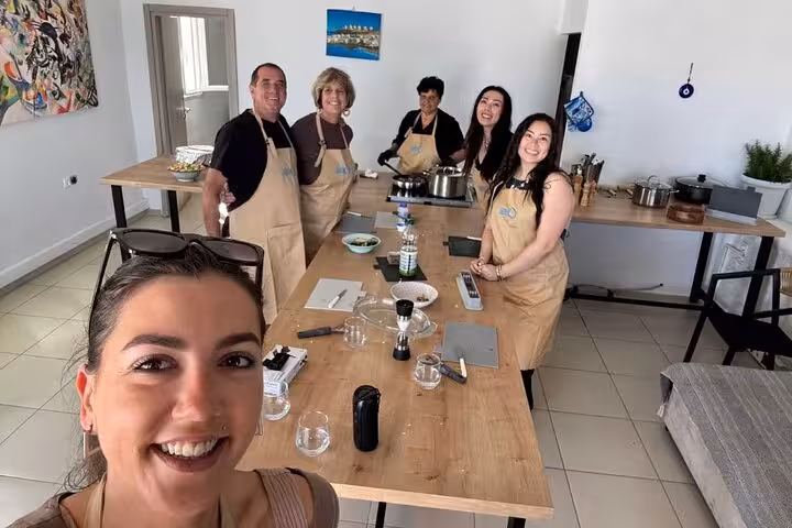 Cruise travelers smiling in a Mykonos cooking class kitchen, wearing aprons and prepping Greek recipes