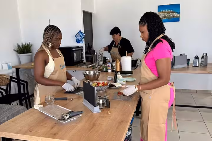 Cruise travelers prep Greek mezze in a Mykonos cooking class, chopping fresh ingredients at a shared kitchen table