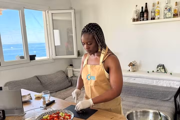 Guest chops fresh vegetables during a small group Mykonian cooking class, with Aegean sea view in Mykonos
