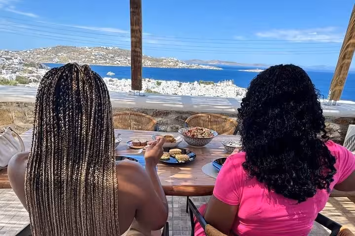 Guests enjoy homemade Greek mezze on a terrace overlooking Mykonos, part of a small group cooking class experience
