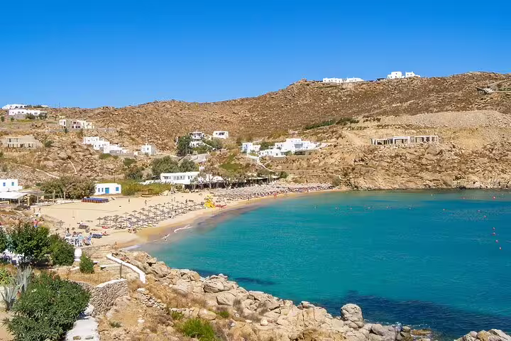 Scenic view of Mykonos countryside with a sandy beach and turquoise waters, perfect for a relaxing tasting experience ride.