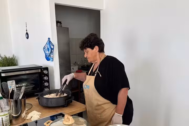 Local host cooking in a Mykonian kitchen during a small group Greek cooking class, preparing traditional island dishes