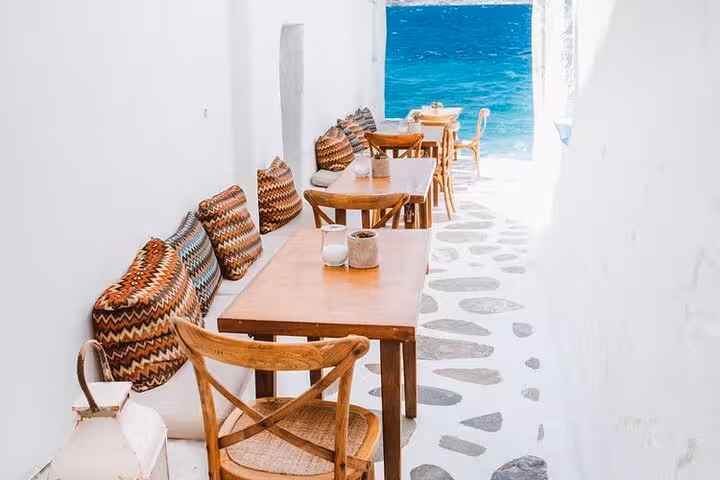 Seaside café alley in Mykonos Chora with blue Aegean view, perfect photo spot on cruise walking tour