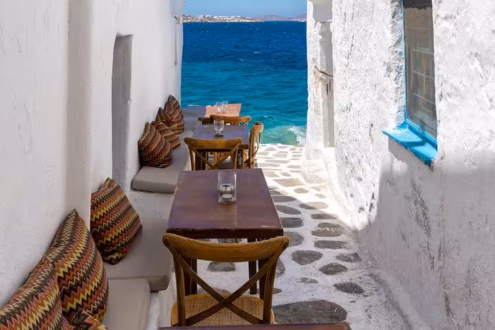 Seaside cafe tables in a whitewashed Mykonos lane overlooking the Aegean, Athens to Mykonos day trip