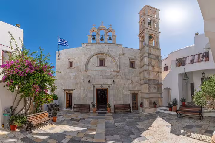 Traditional Mykonos village church courtyard with bell tower and Greek flag, authentic Cyclades culture tour stop