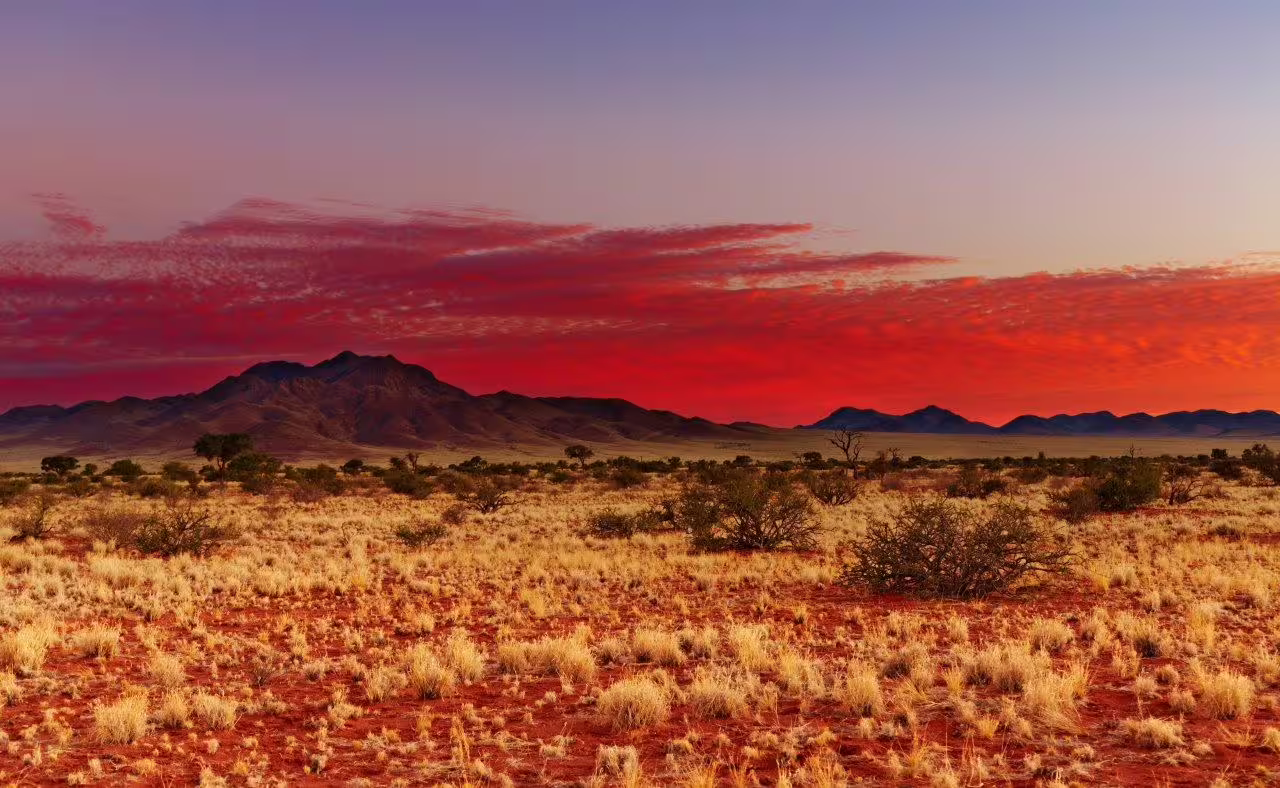 Breathtaking Namibian desert sunset with vivid red skies and mountain silhouettes, perfect for self-drive exploration.