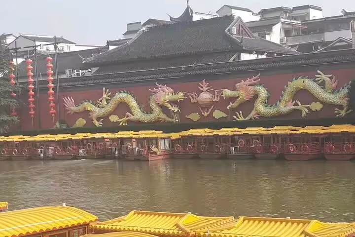 Colorful dragon mural on a building by the Qinghuai River, with traditional boats docked in Nanjing.