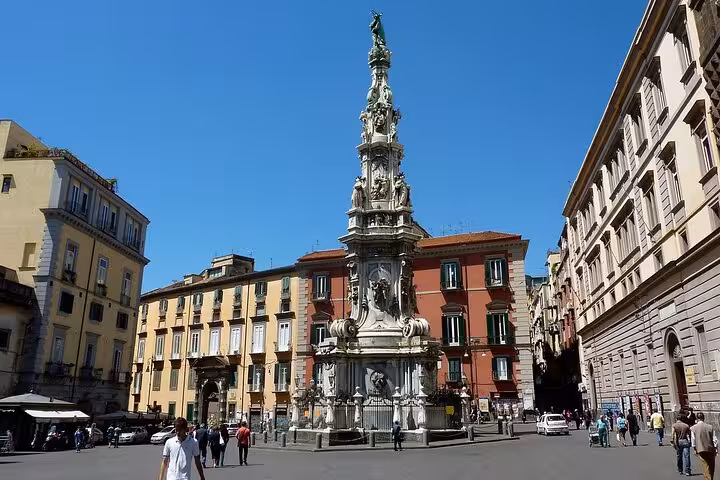 The striking Spire of the Immaculate Virgin stands in a vibrant Naples square, surrounded by historic buildings.
