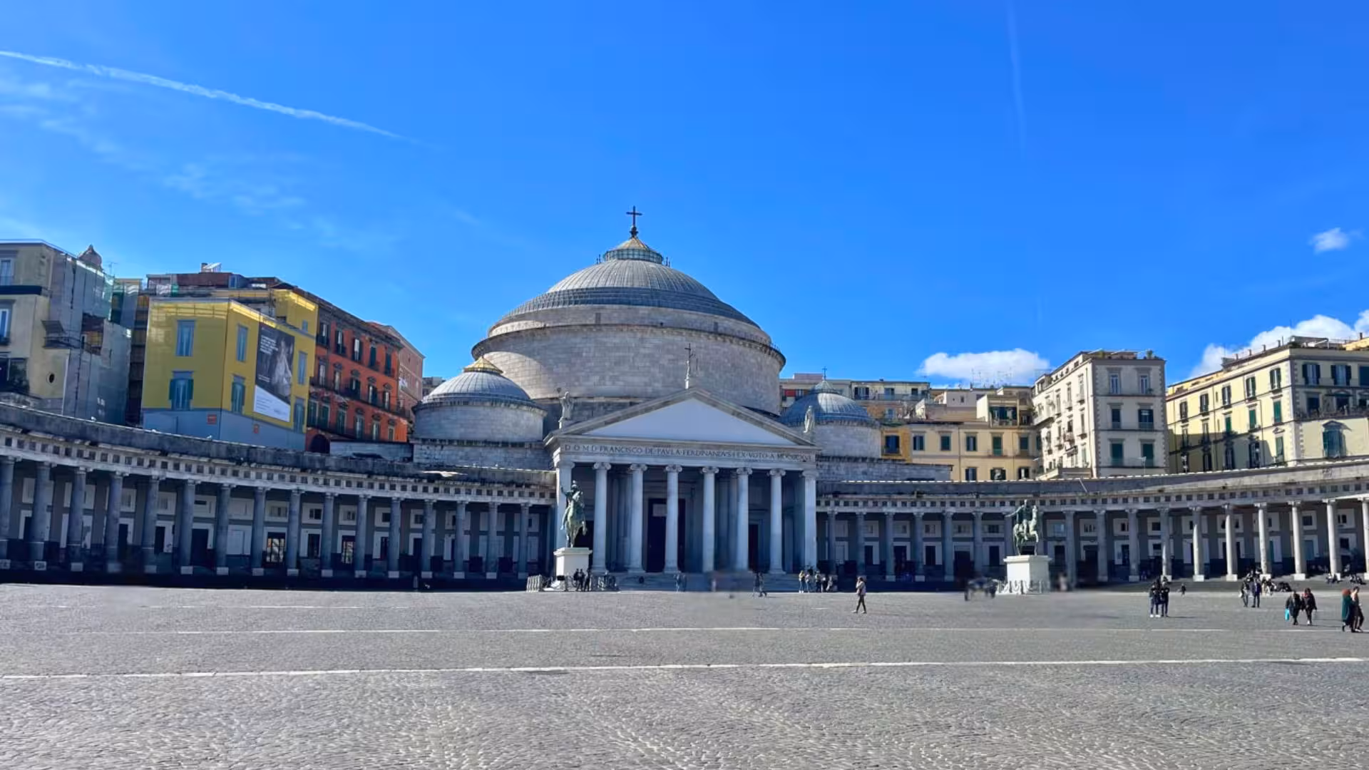 Panoramic view of Plebiscito Square in Naples, featuring the iconic Basilica with vibrant buildings under a clear sky.