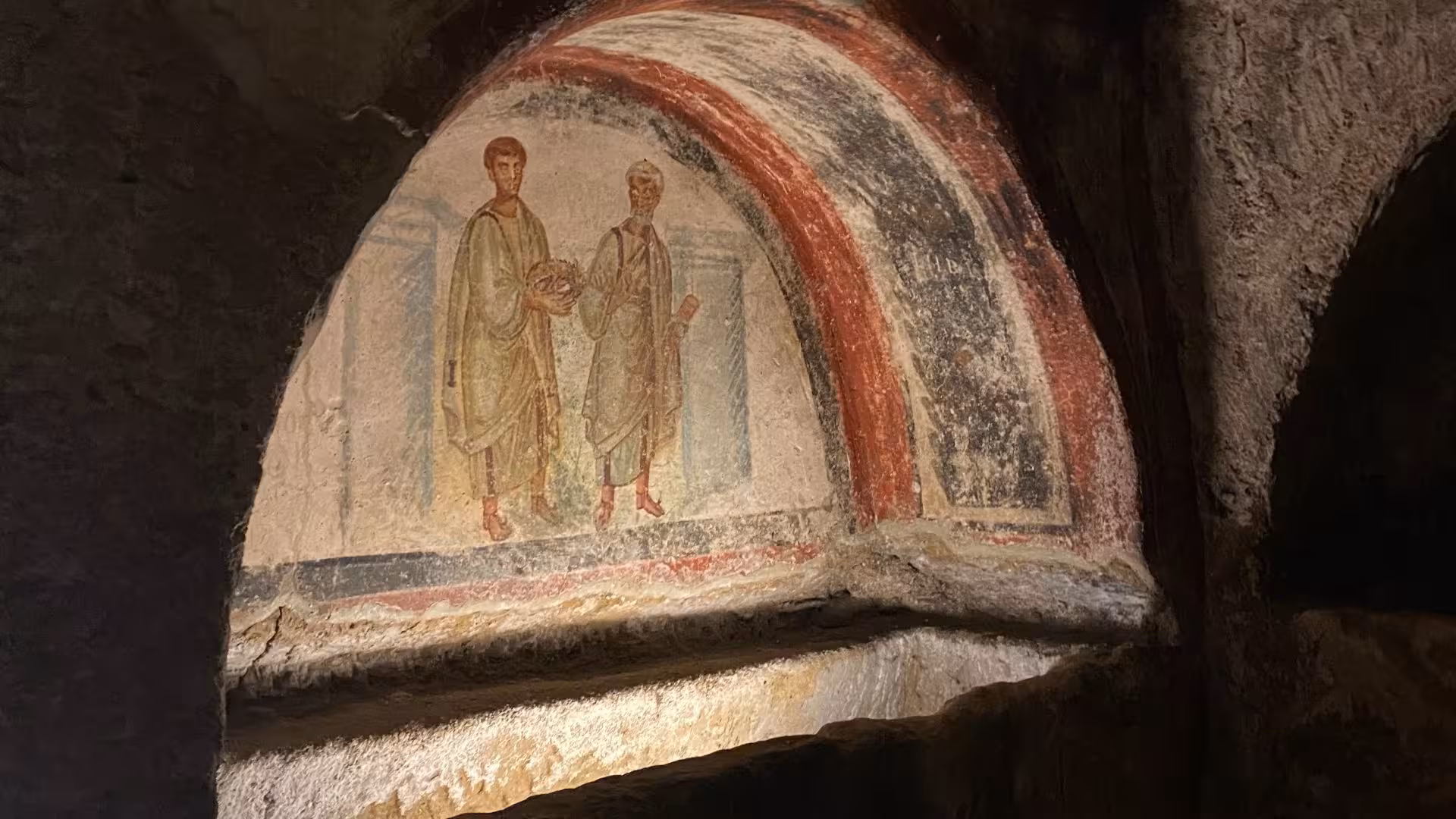 Ancient fresco depicting two figures in the catacombs of Naples' historic Sanità district.