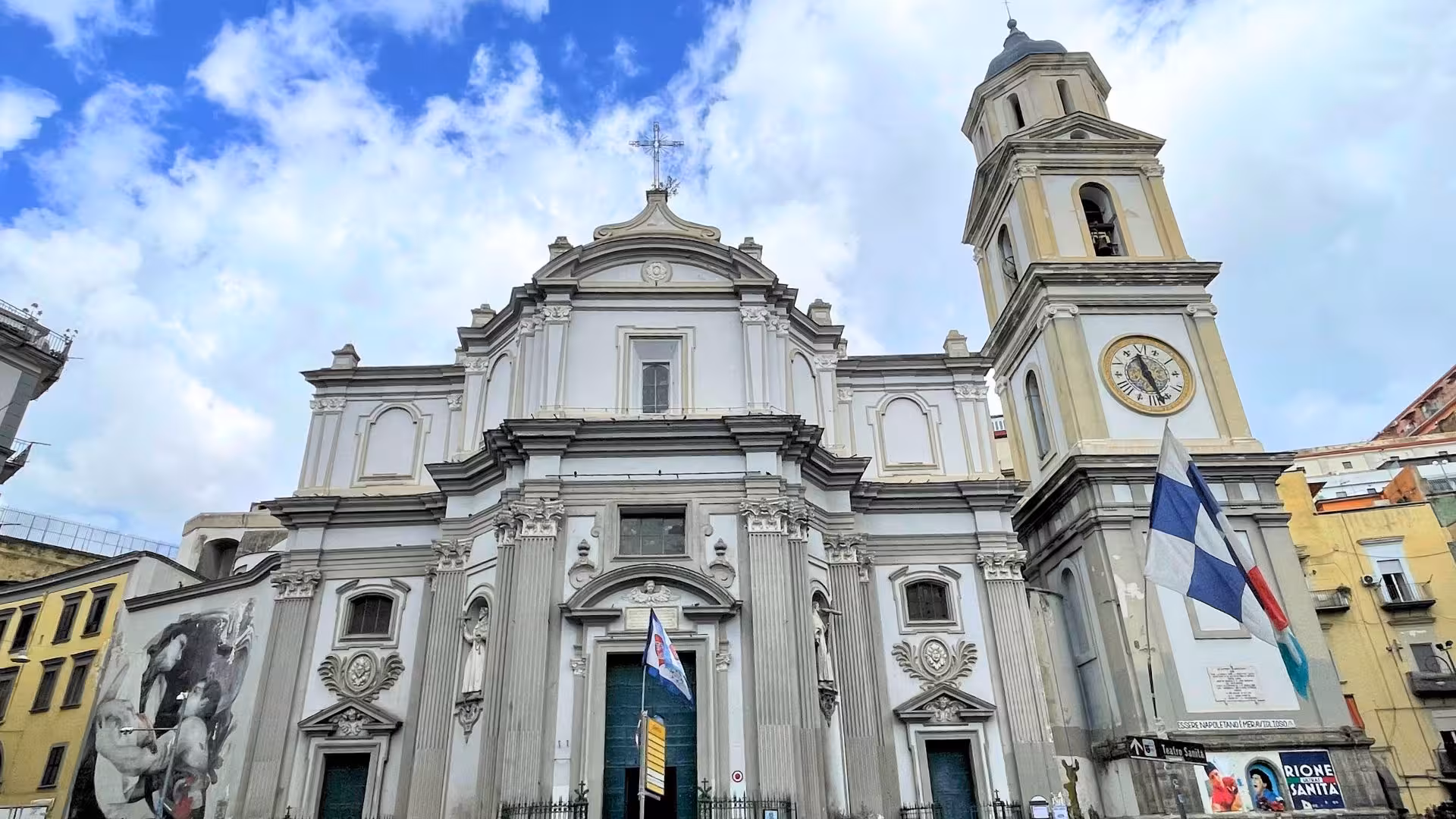Facade of a grand church with clock tower in Naples' Sanità district, showcasing historical charm and cultural heritage.