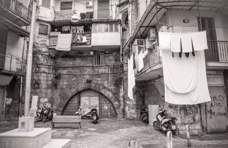 Narrow courtyard in Naples’ Sanità district with hanging laundry, scooters and old stone archway seen on the guided walking tour