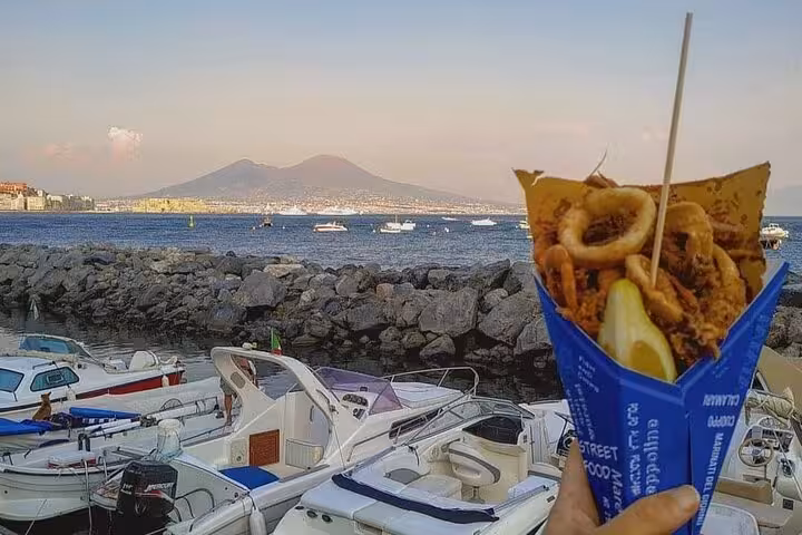 Street food cones with fried seafood against the scenic backdrop of Naples harbor and Mount Vesuvius.