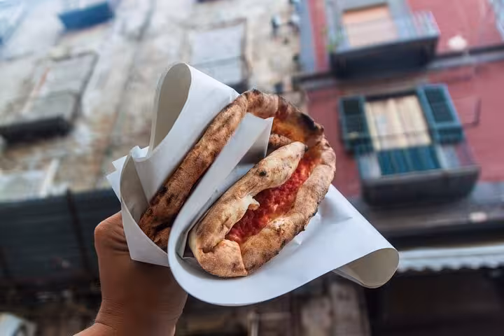 Street food pizza held up against the backdrop of traditional Naples architecture on a walking tour.