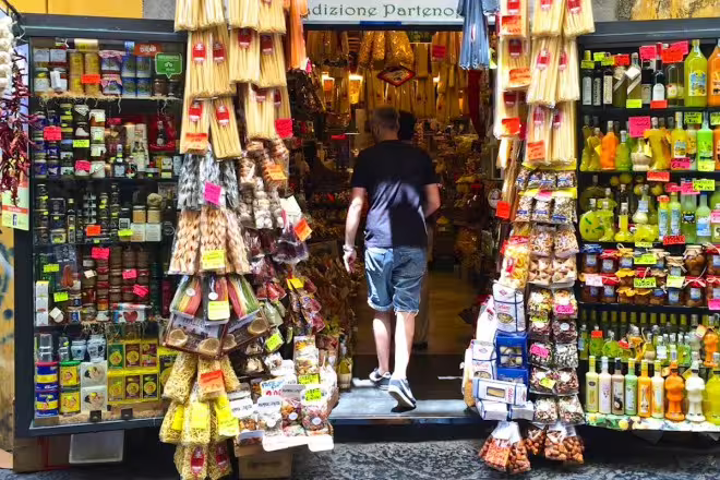 Traveler entering a Naples deli packed with local pasta, spices and snacks on a guided street food tour