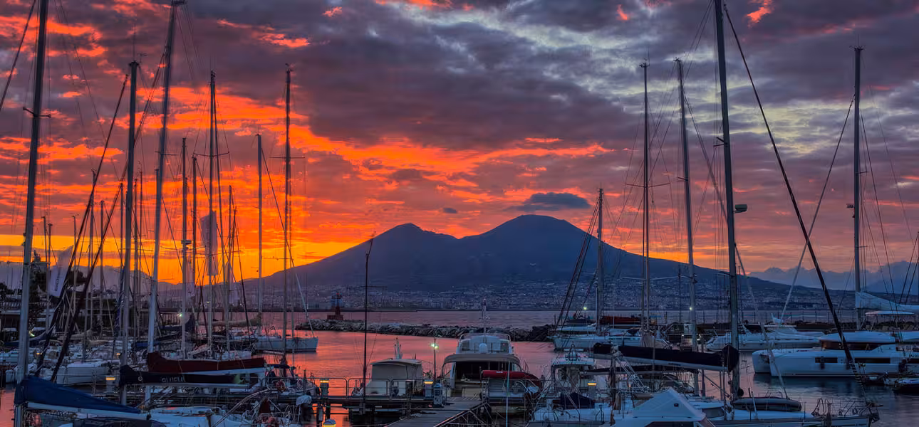 Dramatic sunrise over Naples harbor with sailboats and Mount Vesuvius, perfect for a gulf tour backdrop.