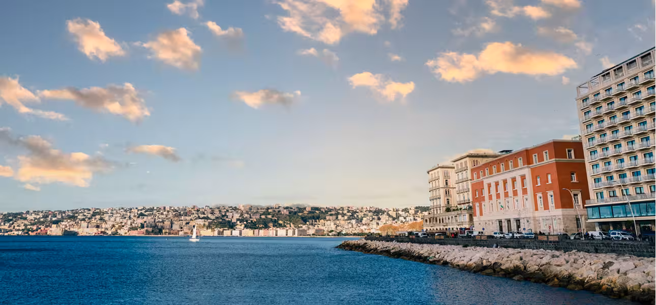 Picturesque coastline of Naples with colorful buildings and calm sea under a morning sky, ideal for a gulf tour.