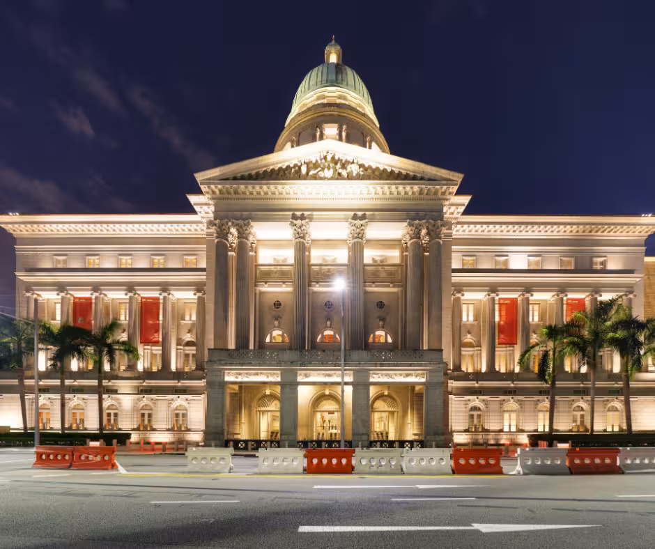 Night view of National Gallery Singapore, a grand neoclassical building beautifully lit with palm trees lining the street.