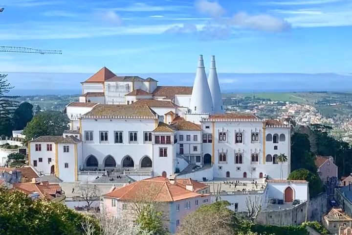 Aerial view of the National Palace of Sintra with its iconic twin chimneys and surrounding lush landscape.