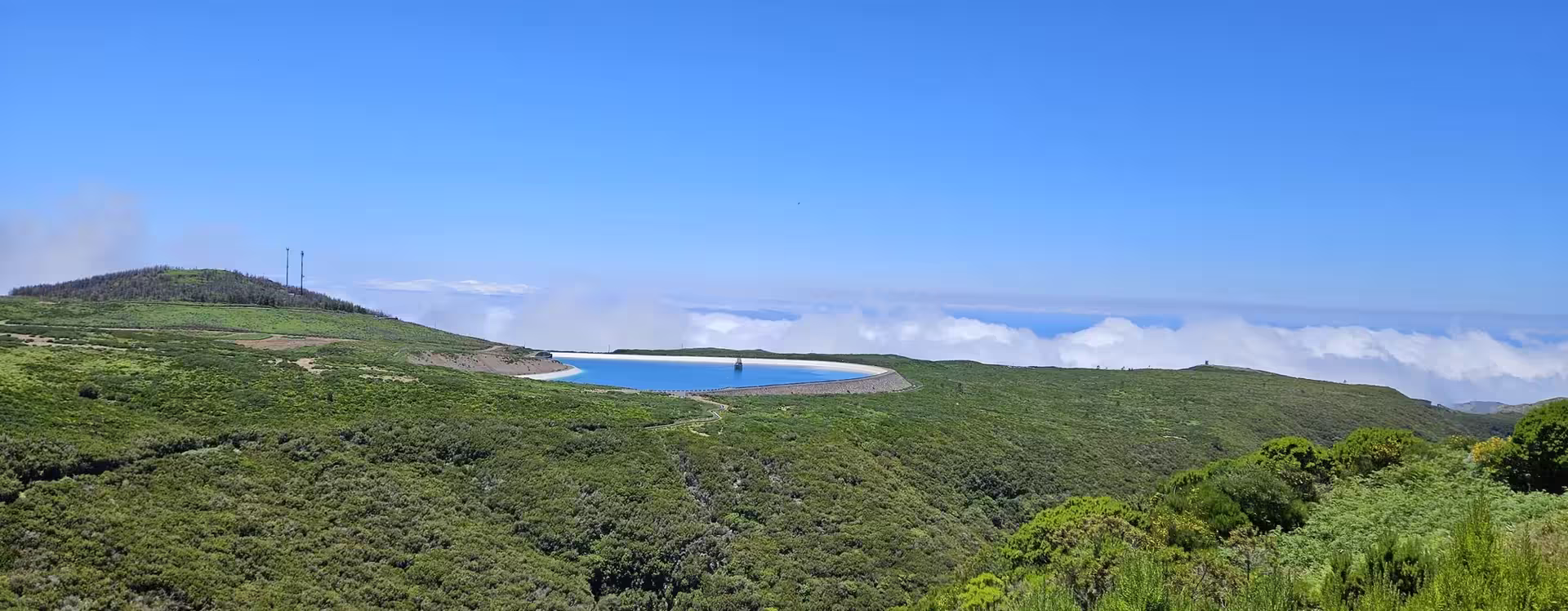 Breathtaking view of a serene reservoir nestled in lush green hills under a clear blue sky, perfect for hikers.