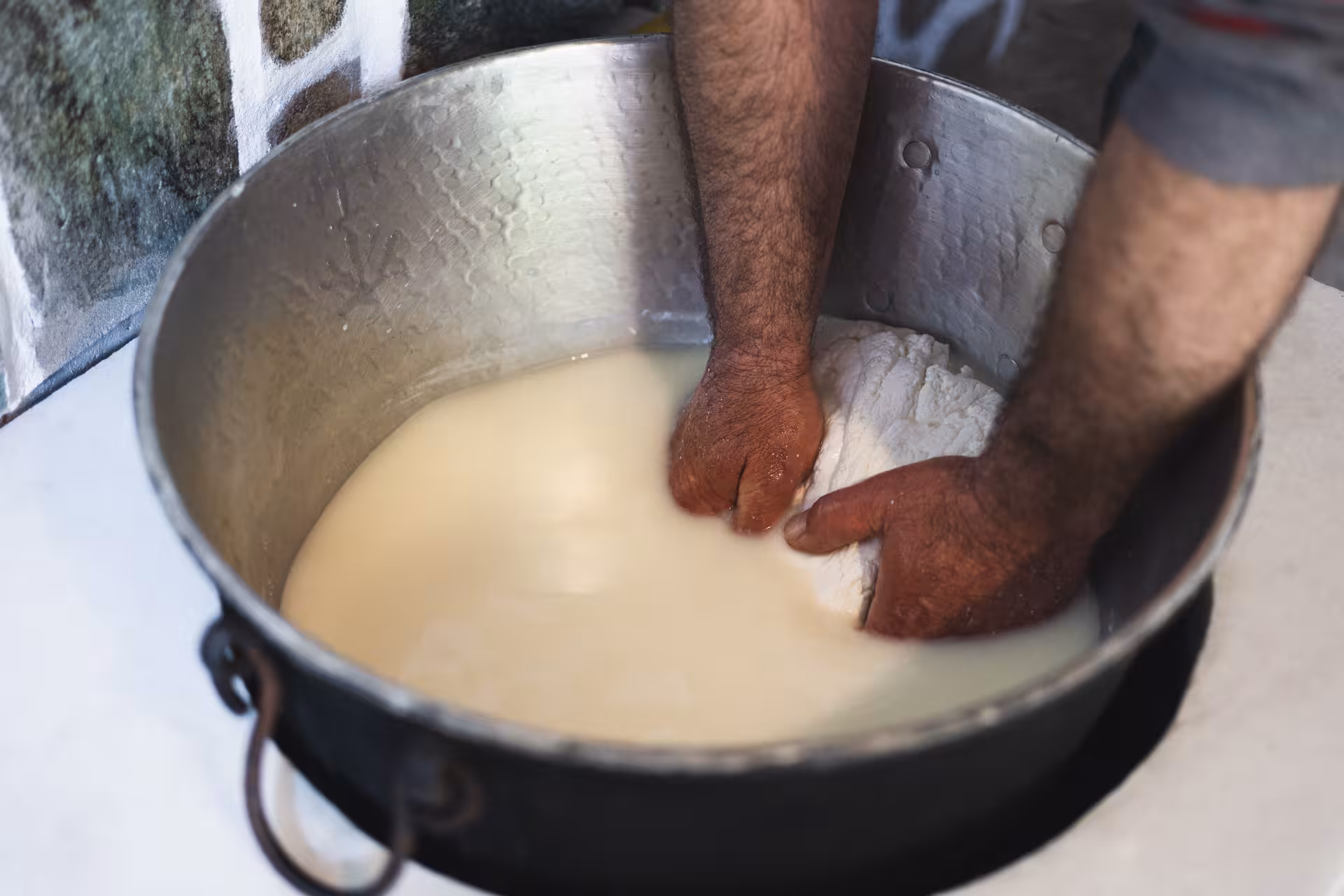 Hands pressing fresh curds in a large pot during the Naxos cheesemaking class with local milk