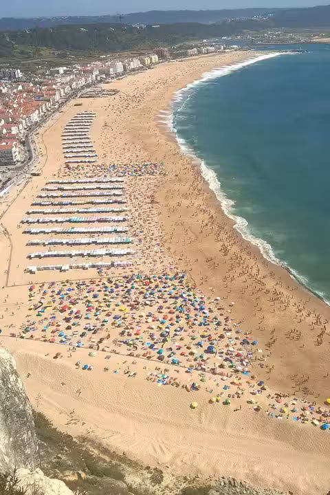 Aerial view of Nazare beach with colorful umbrellas and sunbathers, highlighting a key stop on the Fatima, Nazare, and Obidos tour.