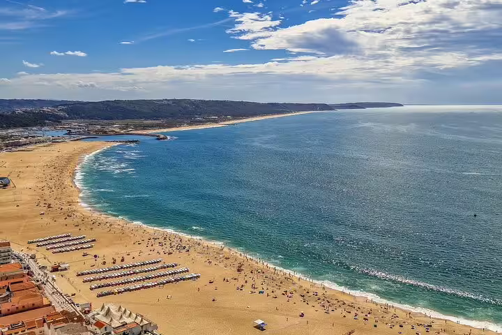 Scenic view of Nazare beach with golden sands and vibrant blue waters, perfect for a day trip on the Fatima, Nazare, and Obidos tour.