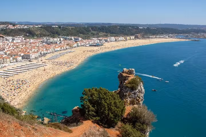 Panoramic view of Nazaré beach, Portugal, with golden sands, turquoise waters, and a vibrant coastal town backdrop.
