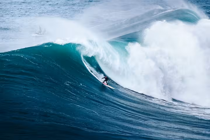 Surfer riding a massive wave in Nazaré, Portugal, famous for its big wave surfing and stunning ocean views.