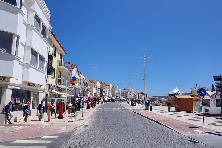 Coastal street scene in Nazaré with vibrant buildings and tourists, part of the Fátima, Nazaré, Batalha, and Óbidos tour.