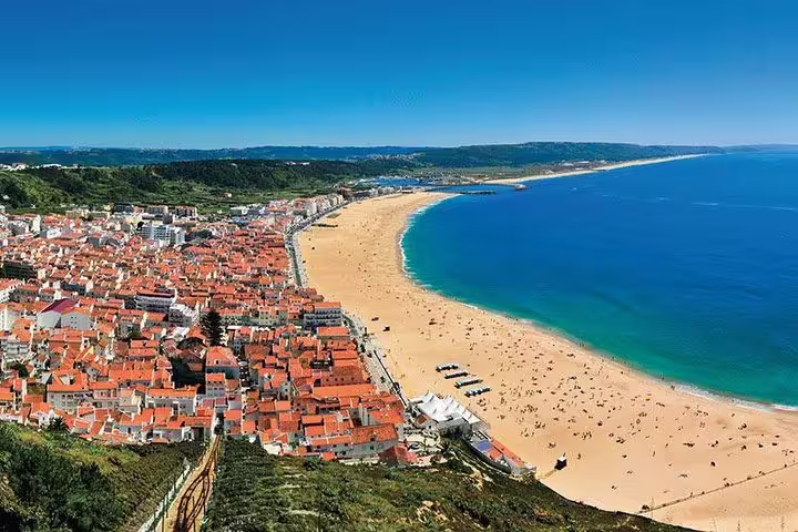 Scenic aerial view of Nazaré's stunning coastline with sandy beaches and vibrant town, featured in Fatima and Óbidos tour.