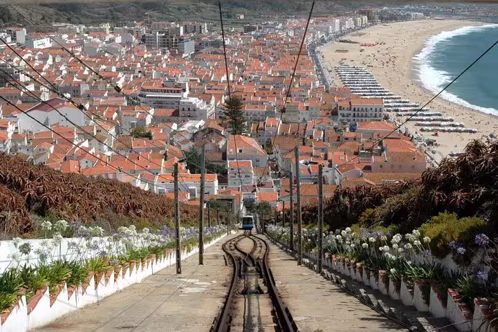 Scenic view of Nazaré's coastline and red-roofed town from a hillside, featuring a funicular railway and beach in Portugal.