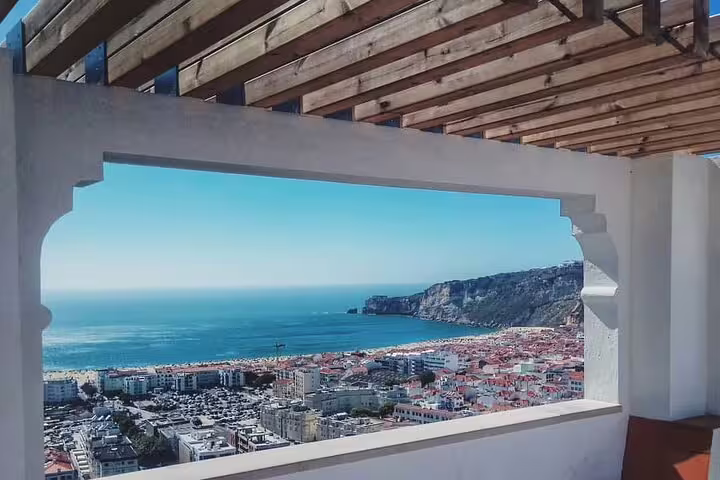 Scenic view of Nazaré's coastline and red-roofed buildings from a terrace, featured in the Fátima, Nazaré, and Óbidos full-day tour.