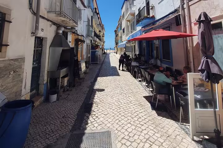 Charming cobblestone street in Nazaré with outdoor café seating, part of the Fátima, Batalha, Nazaré & Óbidos private tour.