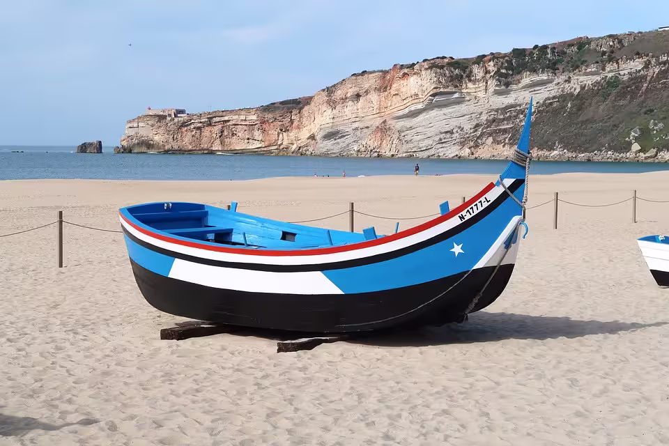 Traditional painted fishing boat on Nazaré beach with cliffs and ocean in the background.