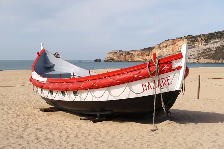 Traditional fishing boat on Nazaré beach with scenic cliffs in the background, featured in a Lisbon day tour to Fátima, Nazaré, and Óbidos.