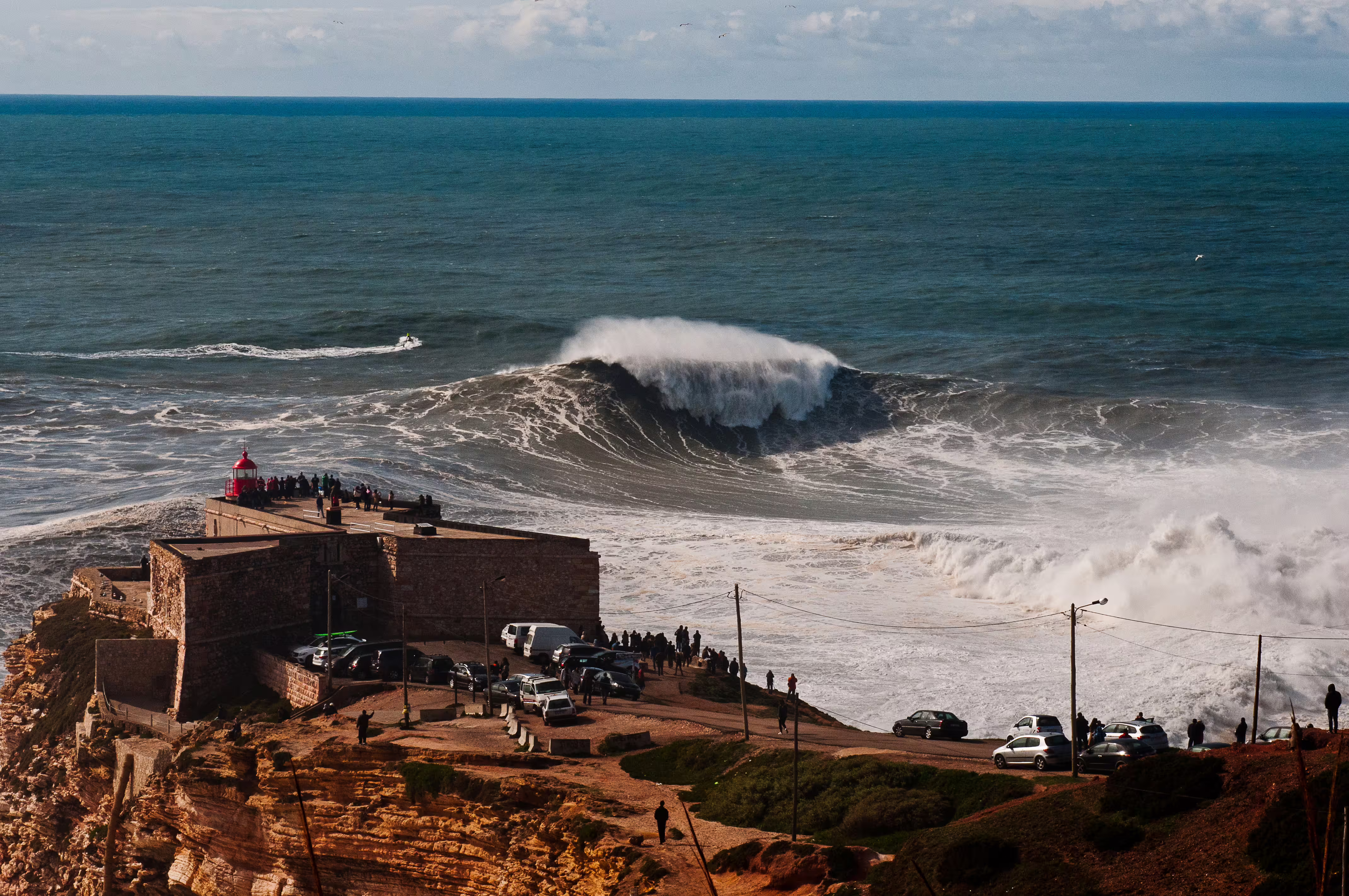 A breathtaking view of giant waves at Nazaré with a scenic lighthouse, perfect for a private tour to explore Portugal's coast.