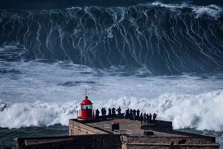 Spectacular view of giant waves crashing near the iconic red lighthouse in Nazaré, Portugal, during the Fatima Nazare and Obidos tour.