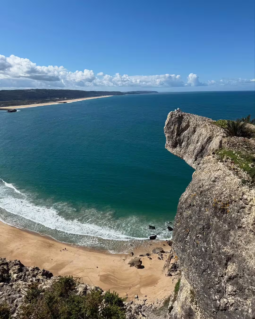 Breathtaking view of Nazaré's coastline with towering cliffs and azure waves, ideal for surf enthusiasts seeking giant wave adventures.