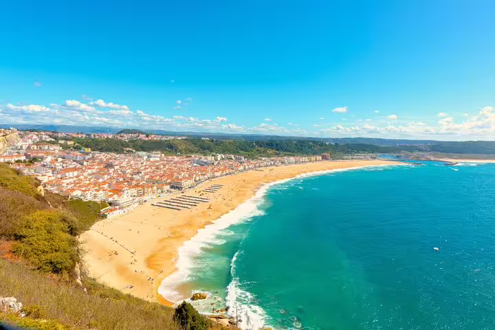 Scenic view of Nazaré's golden beach and vibrant coastline under a clear blue sky, part of Lisbon's day tour itinerary.